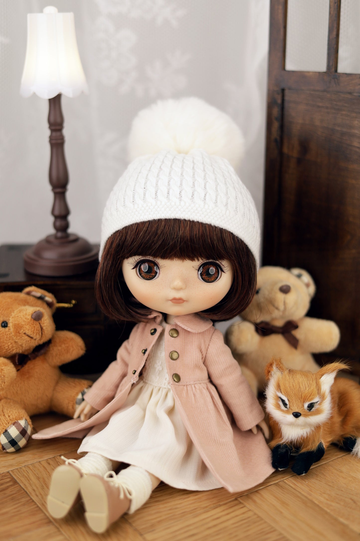 Doll wearing a white coat and hat with teddy bears and a fox in the background
