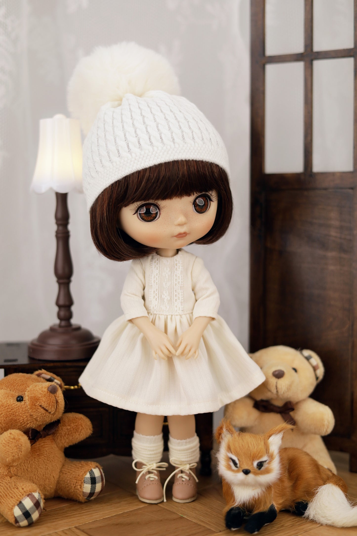 Doll in a white outfit with a white hat surrounded by stuffed animals in a room setting.