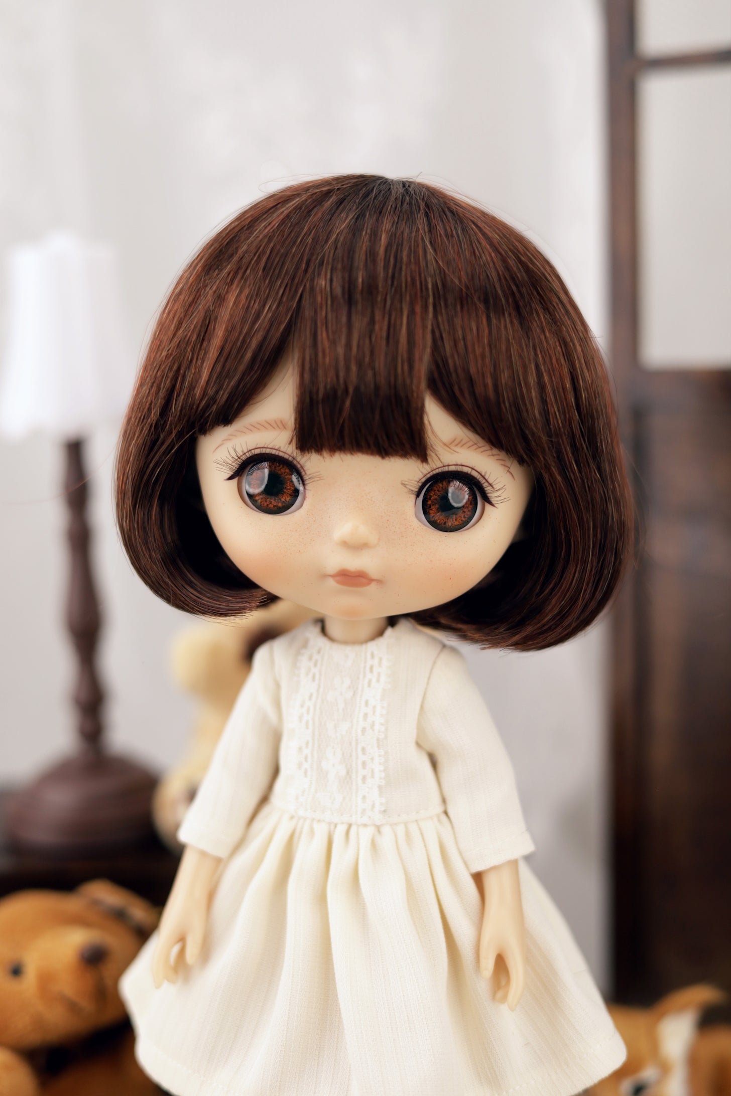 Doll with brown hair and a white dress in a blurred indoor setting