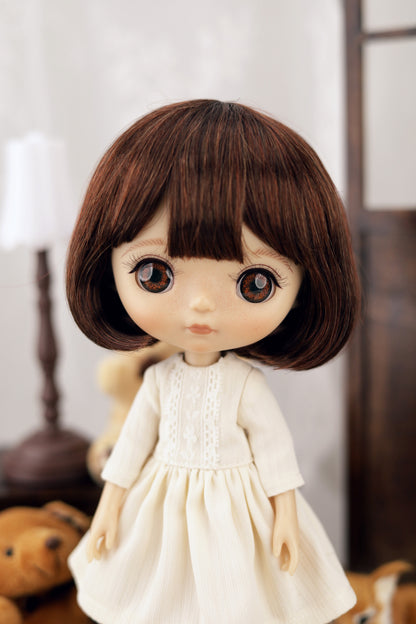 Doll with brown hair and a white dress in a blurred indoor setting